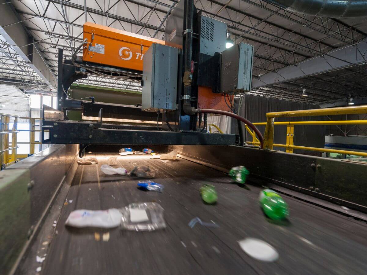 Plastic items move quickly along a conveyor belt toward an optical sorter at a Material Recovery Facility (MRF)